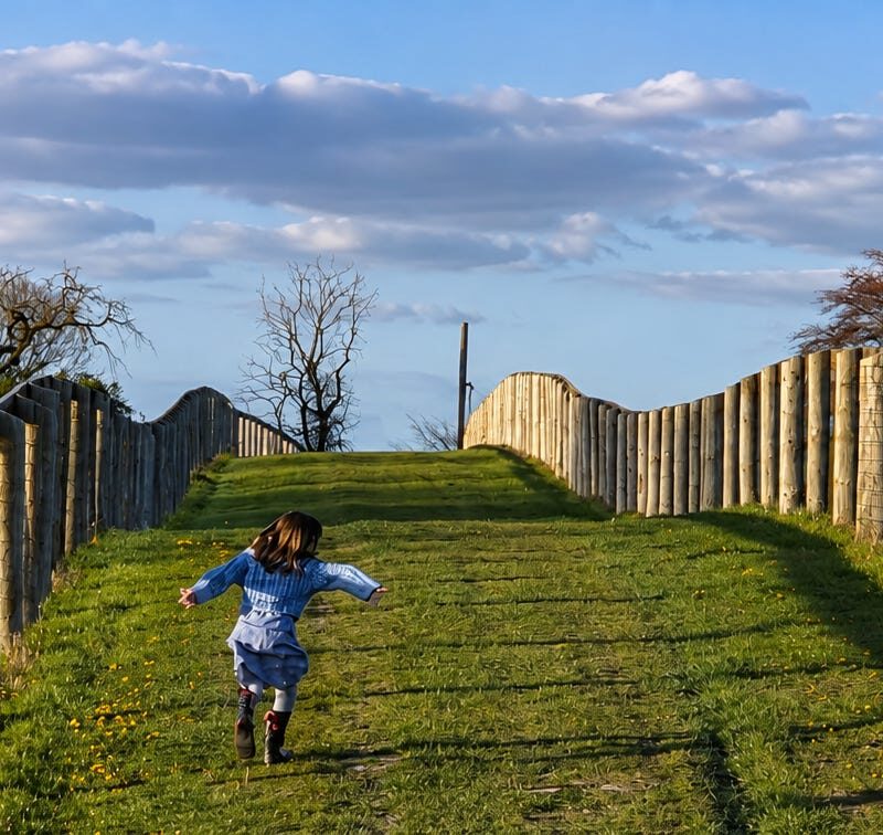 A child running up a fenced grass path through fields near Henley-on-Thames in golden evening light