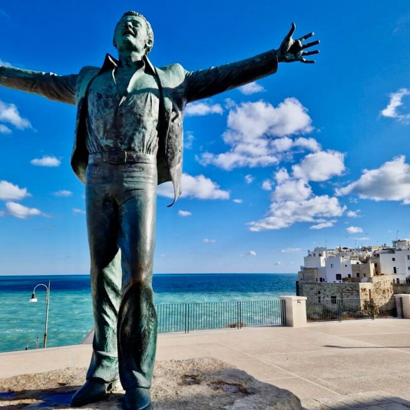 The bronze Domenico Modugno statue in Polignano a Mare, arms thrown wide above the sea
