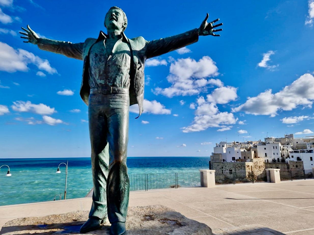 The bronze Domenico Modugno statue in Polignano a Mare, arms thrown wide above the sea